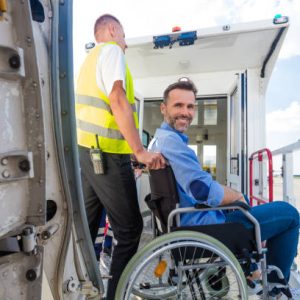Ground service men helping wheelchair passenger to enter on airplane board, they using an elevator. Disabled man smiling at camera.